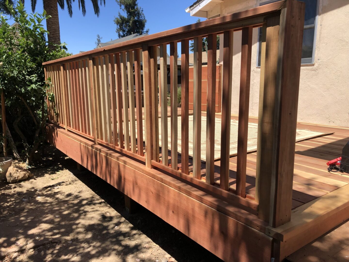 A wooden deck with a railing and palm trees in the background.